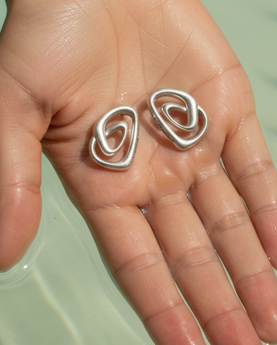 Sterling silver earrings with abstract design on hand over water, yiru.jeweller jewelry